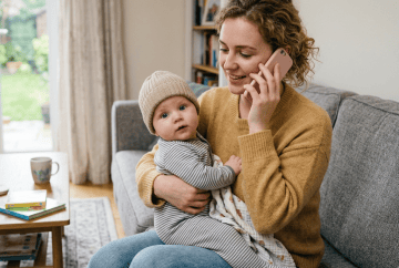 Mother sitting on couch holding baby and talking on phone